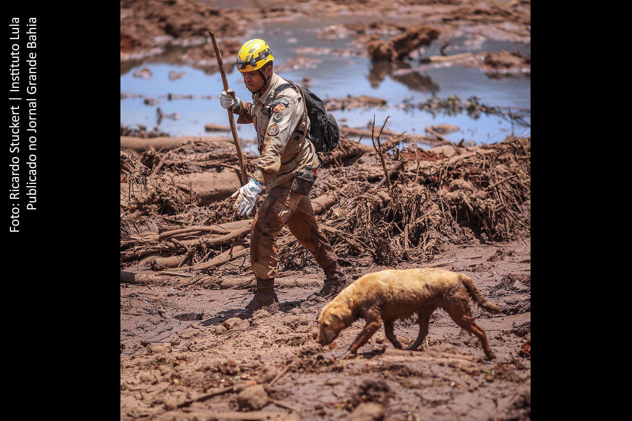 Bombeiros trabalham na localização de vítimas da tragédia no Município de Brumadinho, em Minas Gerais. Imagem apresenta vista panorâmica do dano ambiental causado pelo rompimento da barragem da Mina Córrego do Feijão, de propriedade da empresa Vale, situada em Brumadinho, Minas Gerais. Degradação ambiental compromete Rio Paraopeba. Tragédia é avaliada como um ato de genocídio contra a população e a natureza.
