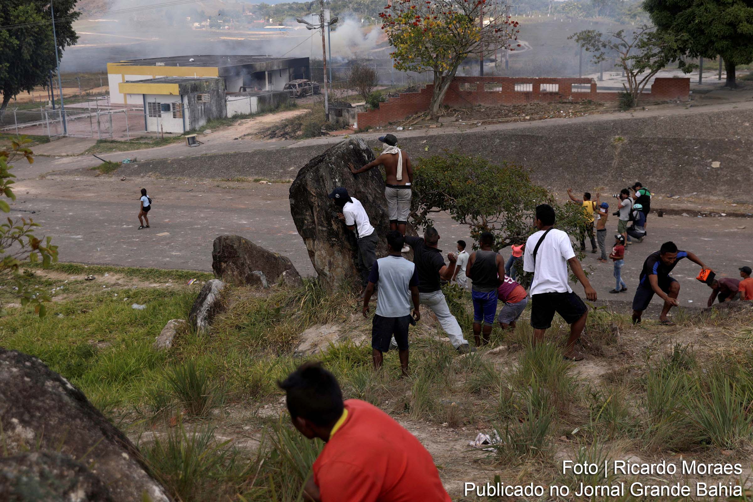 Pessoas se escondem atrás de uma rocha durante confrontos na fronteira venezuelana, em Pacaraima (RR)