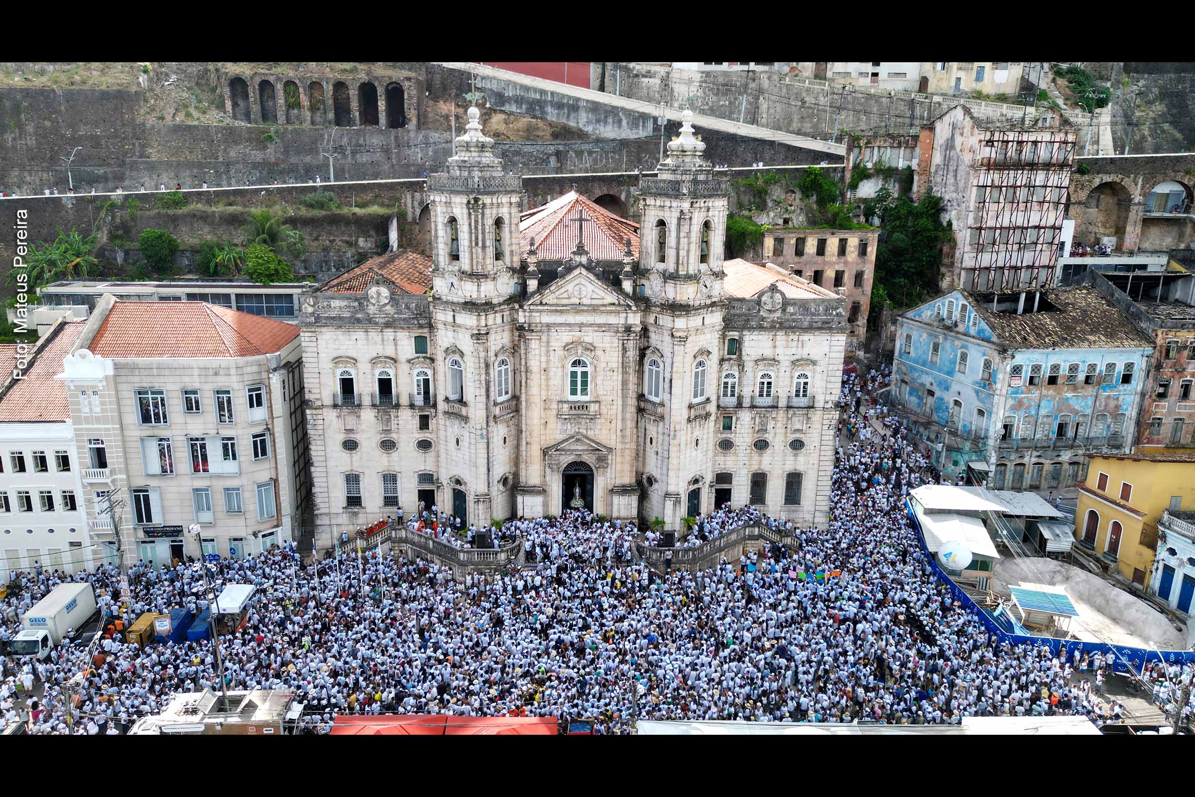 Vista aérea da Igreja de Nossa Senhora da Conceição da Praia, durante início dos festejos da Lavagem do Bonfim de 2024. Cortejo colorido e vibrante marca o trajeto da Imagem do Senhor do Bonfim, com grupos culturais, bandas e artistas, ressaltando a riqueza da diversidade na festa.