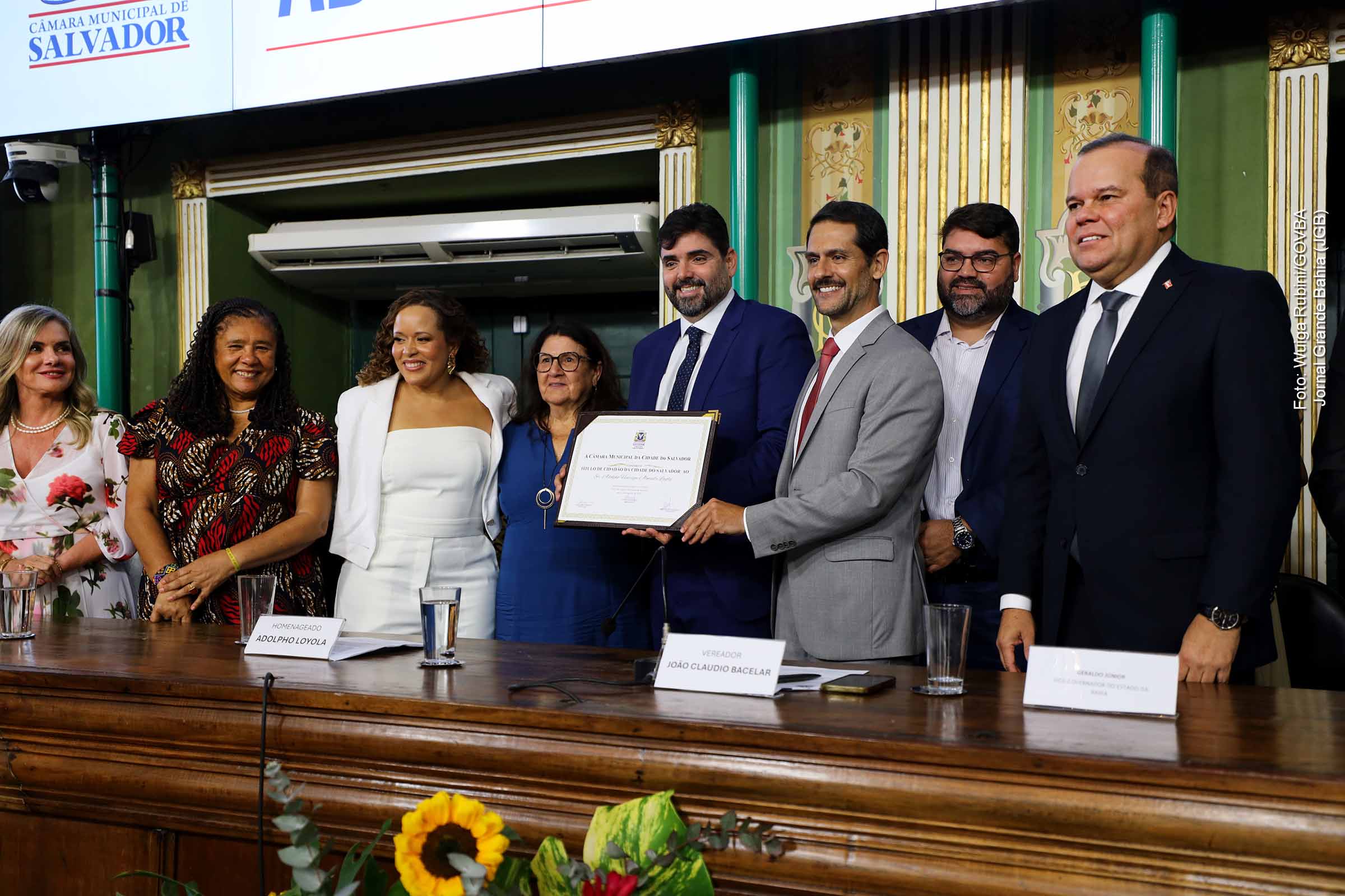 Na quinta-feira (11/09/2025), a Câmara Municipal de Salvador concedeu o título de cidadão soteropolitano ao secretário estadual de Relações Institucionais, Adolpho Loyola. O ato contou com a presença do vice-governador Geraldo Júnior, que destacou a relevância da homenagem e a trajetória do homenageado no serviço público. A solenidade reuniu autoridades, familiares e representantes da sociedade civil.
